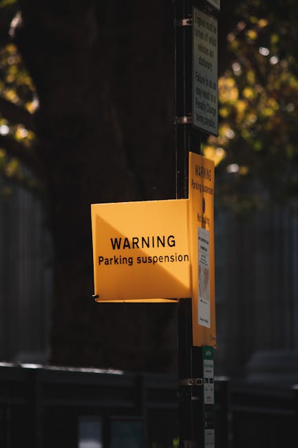Close-up of three traffic and parking restriction signs mounted on a yellow wall, including a no stopping sign, a tow-away zone icon, and a vehicle weight limit sign. The signs are positioned in the u